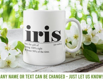 May include: White ceramic mug with a black graphic that says "iris" and defines the word as "has the gift of being 100% right at least 50% of the time." The mug is sitting on a white and brown placemat with white flowers.