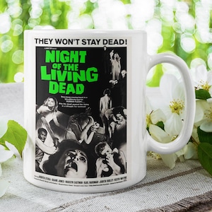 May include: White ceramic mug featuring a black and white movie poster for "Night of the Living Dead." The poster has green and white text, with images of people. The mug has a large handle.