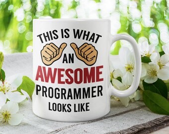May include: White ceramic coffee mug with a black and red design that says "This is what an awesome programmer looks like". The mug has two thumbs up symbols on either side of the word "an".