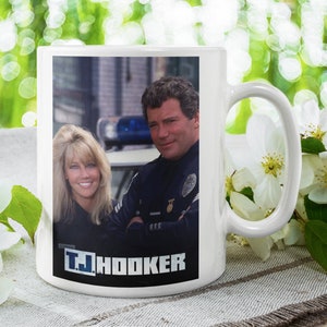 Puede incluir: Taza de cerámica blanca con una imagen a color de dos personas con uniformes de policía. La taza tiene el texto "T.J. HOOKER" impreso en la parte inferior.