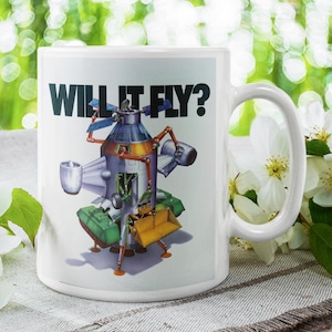 May include: White ceramic mug featuring a retro-style illustration of a spacecraft with the text "WILL IT FLY?" in black. The spacecraft is depicted in shades of blue, orange, and green. The mug has a large handle.