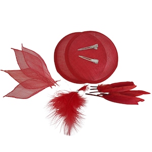 May include: A collection of red hair accessories, including a small hat with two silver barrettes, a cluster of red feathers, and a decorative leaf-shaped piece. The items are arranged on a white background.