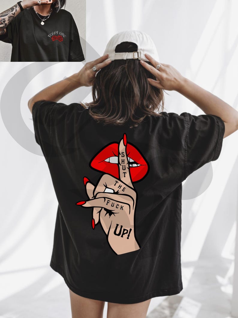 Peut inclure: T-shirt noir avec un motif au dos repr&eacute;sentant des l&egrave;vres rouges, un doigt faisant chut, et les mots "SHUT THE FUCK UP!". Le devant du t-shirt pr&eacute;sente un petit motif de rose rouge avec du texte. Une casquette de baseball blanche est port&eacute;e.