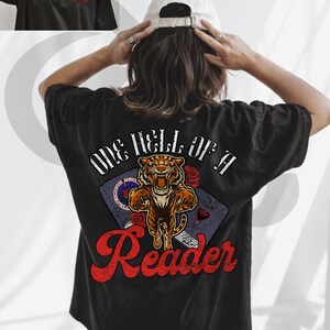 Puede incluir: Camiseta negra con un gr&aacute;fico en la espalda. El gr&aacute;fico dice "ONE HELL OF A Reader" en escritura roja, con un tigre, rosas y un libro. La parte delantera de la camiseta tiene el texto "Teddy Rose" en rojo.