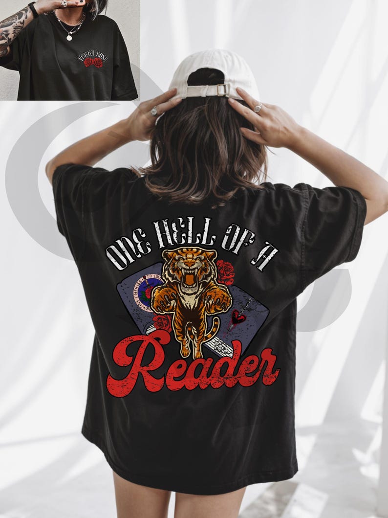 Puede incluir: Camiseta negra con un gr&aacute;fico en la espalda. El gr&aacute;fico dice "ONE HELL OF A Reader" en escritura roja, con un tigre, rosas y un libro. La parte delantera de la camiseta tiene el texto "Teddy Rose" en rojo.