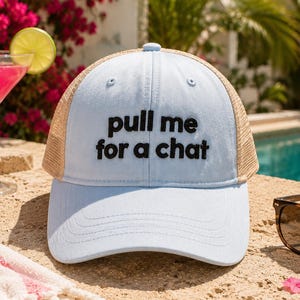 Puede incluir: Una gorra tipo trucker de color azul claro con malla trasera color canela y visera curva. El panel frontal presenta el texto bordado en negro "pull me for a chat" en una fuente negrita sin remates. La gorra tiene una corona estructurada y un botón.