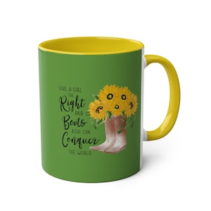 以下が含まれることがあります： 黄色の縁取りと取っ手のある緑色のセラミックマグカップ。マグカップには、ひまわりと「Give a girl the right pair of boots & she can conquer the world.」というテキストが書かれた、茶色のカウボーイブーツのグラフィックが描かれています。