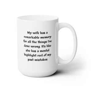 Può includere: Una tazza da caffè in ceramica bianca con testo nero che recita: "Mia moglie ha una memoria straordinaria per tutte le cose che ho fatto male. È come se avesse un rullo di evidenziazione mentale dei miei errori passati."