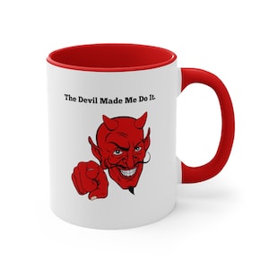 May include: White ceramic mug with a red rim and handle. The mug features a red cartoon devil with horns and a mischievous grin, pointing at the viewer. The text "The Devil Made Me Do It." is printed in black above the devil.