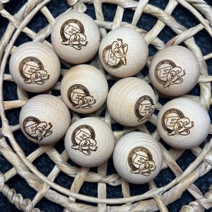 Peut inclure: Onze boules en bois clair, chacune avec un logo gravé brun foncé représentant les lettres "E" et "S" avec un personnage de dessin animé. Les boules sont disposées dans un panier tressé de forme circulaire.
