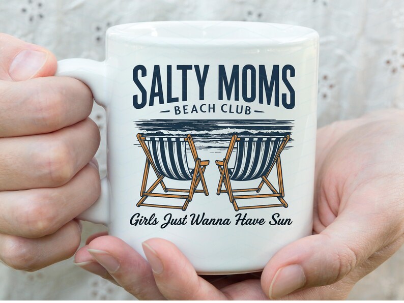 May include: White ceramic mug with a black and white illustration of beach chairs and the text "Salty Moms Beach Club - Girls Just Wanna Have Sun".