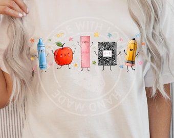 May include: A white t-shirt featuring a graphic print of five anthropomorphic school supplies: a blue crayon, a red apple, a pink ruler, a black and white composition notebook, and a yellow pencil, all with smiling faces and thin black limbs.