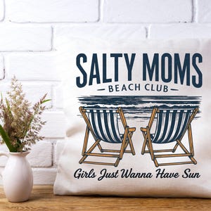 May include: White cushion with the text "Salty Moms Beach Club" and an illustration of two deckchairs with the text "Girls Just Wanna Have Sun" below.