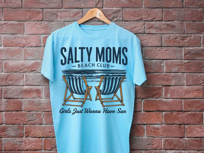 May include: Light blue t-shirt with a graphic design of two beach chairs and the text "Salty Moms Beach Club" and "Girls Just Wanna Have Sun".