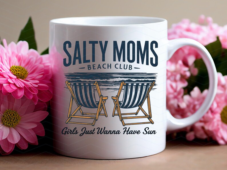 May include: White ceramic mug featuring a design of two deckchairs and the text "Salty Moms Beach Club - Girls Just Wanna Have Sun".