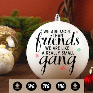 May include: A white Christmas ornament with the text "WE ARE MORE THAN friends WE ARE LIKE A REALLY SMALL gang". The ornament is surrounded by other ornaments and greenery, with a red and gold color scheme.