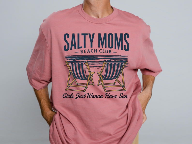 May include: A pink t-shirt with the text "Salty Moms - Beach Club - Girls Just Wanna Have Sun" and a graphic of two deckchairs.