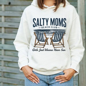 May include: A white hoodie with a graphic design that says "Salty Moms Beach Club" with two beach chairs and the text "Girls Just Wanna Have Sun".