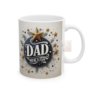 May include: White ceramic mug with a gold and black design. The design features a large gold star, the word "DAD" in a black circle, and the text "You're a star" below. The background is beige with gold stars.
