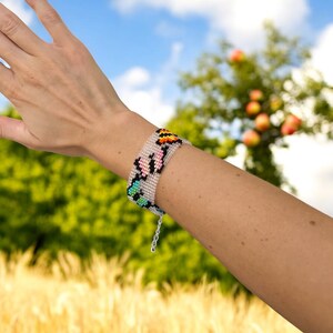 May include: A beaded bracelet with a colorful butterfly design. The bracelet is made with small, colorful beads and has a silver clasp.