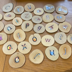 May include: Wooden circles with letters of the alphabet printed on them. The letters are in various colours and fonts. The circles are arranged in a random pattern on a wooden surface.