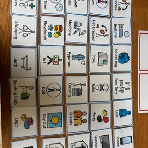 May include: A collection of rectangular visual communication cards with blue borders, each featuring a simple line drawing and a text label. The cards depict daily activities, people, and objects such as doctors, shopping, bath, reading, lego, ipad, home time, playdough, art, dad, day out, hospital, physio, medicine, pyjamas, cooking, friends, church, mum, get dressed, story, toilet, party, television, undress, bedtime, school bag, free time, coat, and phone.