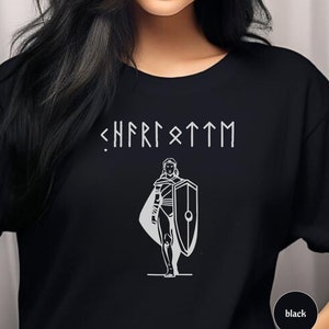 May include: Black t-shirt featuring a white graphic of a woman holding a shield and the text "<HFRISTTM" in a runic font.