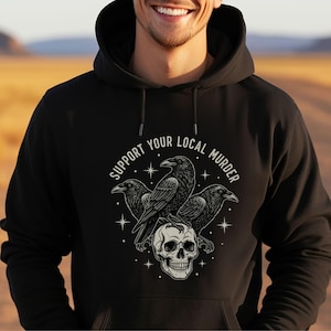 May include: Black hoodie featuring a graphic of three crows perched on a skull, with the text "SUPPORT YOUR LOCAL MURDER" in a circular design. The design is in shades of gray and white.