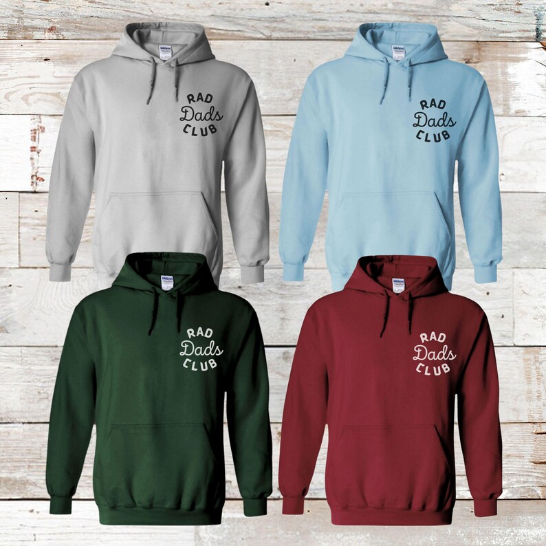 May include: Four hooded sweatshirts in different colors: gray, light blue, green, and maroon. Each sweatshirt has a white graphic on the front that says "Rad Dads Club" in a retro font.