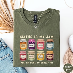 May include: A military green t-shirt featuring the phrase "MATHS IS MY JAM" and illustrations of jam jars with maths terms such as "Problem Solving" and "Formulas". The text "AND I'M HERE TO SPREAD IT!" is also printed on the shirt.
