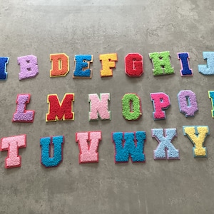 May include: A set of 26 colourful felt letters, each letter is a different colour and is in a blocky, uppercase font. The letters are arranged in alphabetical order.