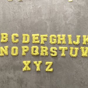 May include: Yellow felt alphabet letters, A through Z, on a grey background.