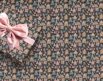 May include: A gift wrapped in dark paper featuring a repeating pattern of small houses and trees in shades of pink, blue, and tan, accented with a large, soft, light pink velvet ribbon tied in a bow on the upper left corner of the package.
