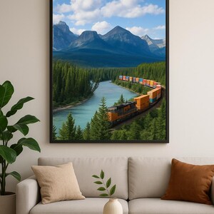 May include: A framed landscape print featuring a train winding along a river through a forest, with mountains in the background. The train cars are various colors, and the sky is blue with clouds. The print is displayed above a beige sofa.