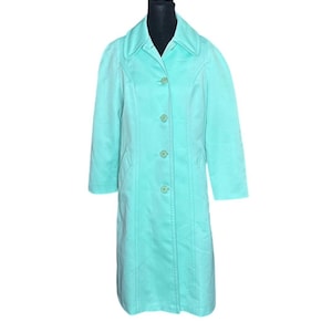 May include: A light turquoise, knee-length coat with a notched collar and button-up closure. The coat has long sleeves and a tailored fit, with vertical seams adding structure. The buttons match the coat's color.
