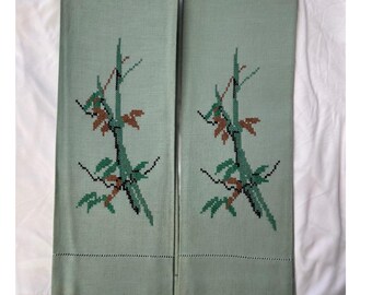 Puede incluir: Dos toallas de mano rectangulares de color verde claro con tallos de bambú bordados en verde, marrón y negro. Las toallas tienen un borde cosido a lo largo del borde inferior. Las toallas se muestran sobre una superficie blanca.