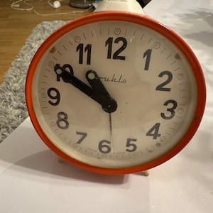May include: A red and white alarm clock with black hands and numbers. The clock face reads "ruhla" and "made in GDR".