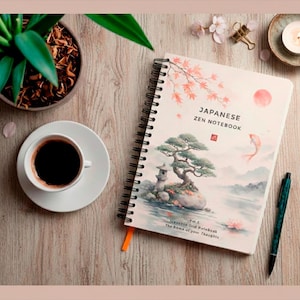 Puede incluir: Un cuaderno de espiral con el texto "Japanese Zen Notebook" y una ilustración de un jardín japonés. Una taza de café, un bolígrafo y una pequeña planta en maceta también están sobre la superficie de madera.