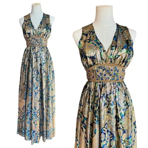 Puede incluir: Vestido largo sin mangas con escote en V. El vestido presenta un estampado de cachemira dorado, azul y verde. La cintura está ceñida con una banda de cuentas doradas y azules. La tela tiene un brillo metálico, dándole un aspecto vintage.