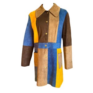 Puede incluir: Un abrigo de ante con diseño de bloques de color. El abrigo tiene cuello, mangas largas y botones dorados. La combinación de colores incluye tonos de marrón, azul, amarillo y beige. El abrigo mide aproximadamente 90 cm de largo.
