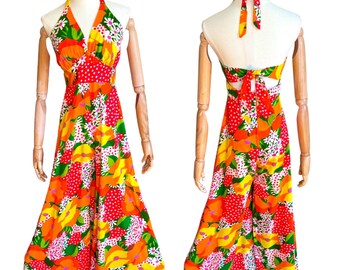 May include: A halter-style jumpsuit with a vibrant floral print featuring orange, yellow, green, and red flowers on a white background. The jumpsuit has a wide-leg silhouette and a tie closure at the back.