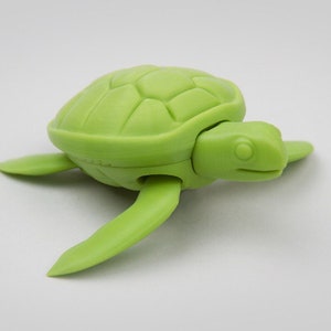 May include: A green plastic toy turtle with a detailed shell and a small head. The turtle is in a swimming position with its flippers extended.