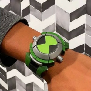 May include: A green and silver toy watch with a green symbol on the face. The watch is worn on a person's wrist.