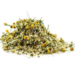 May include: Dried chamomile flowers in a pile on a white background. The flowers are a pale yellow color with green stems.