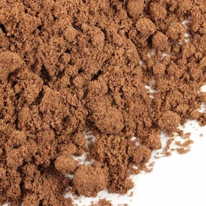 May include: Close-up of a pile of ground allspice, a brown spice with a slightly reddish hue. The spice is finely ground and has a rough texture.