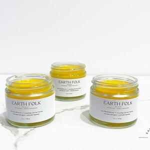 May include: Three small glass jars of yellow facial balm with white labels that read "EARTH FOLK" and "Sea Buckthorn + Rosehip Facial Balm".