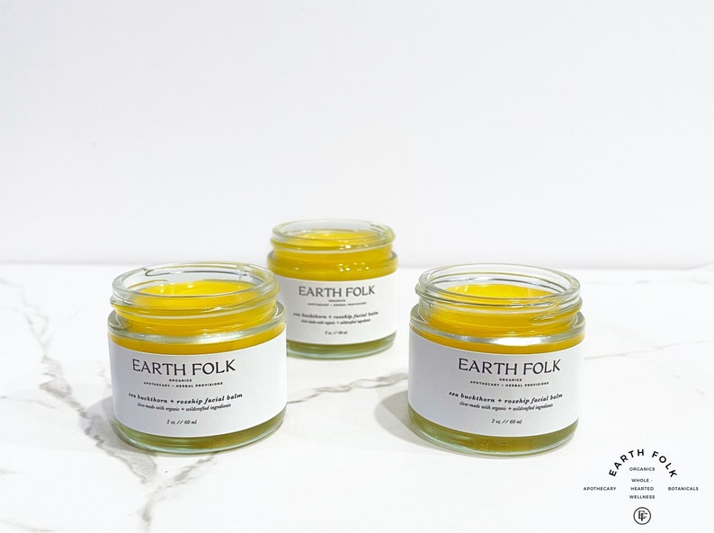 May include: Three small glass jars of yellow facial balm with white labels that read "EARTH FOLK" and "Sea Buckthorn + Rosehip Facial Balm".