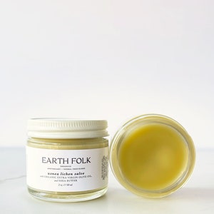 May include: Two glass jars of Earth Folk usnea lichen salve. One jar is closed with a white lid, the other is open, revealing a yellow balm. The label reads "usnea lichen salve with organic extra virgin olive oil and shea butter."