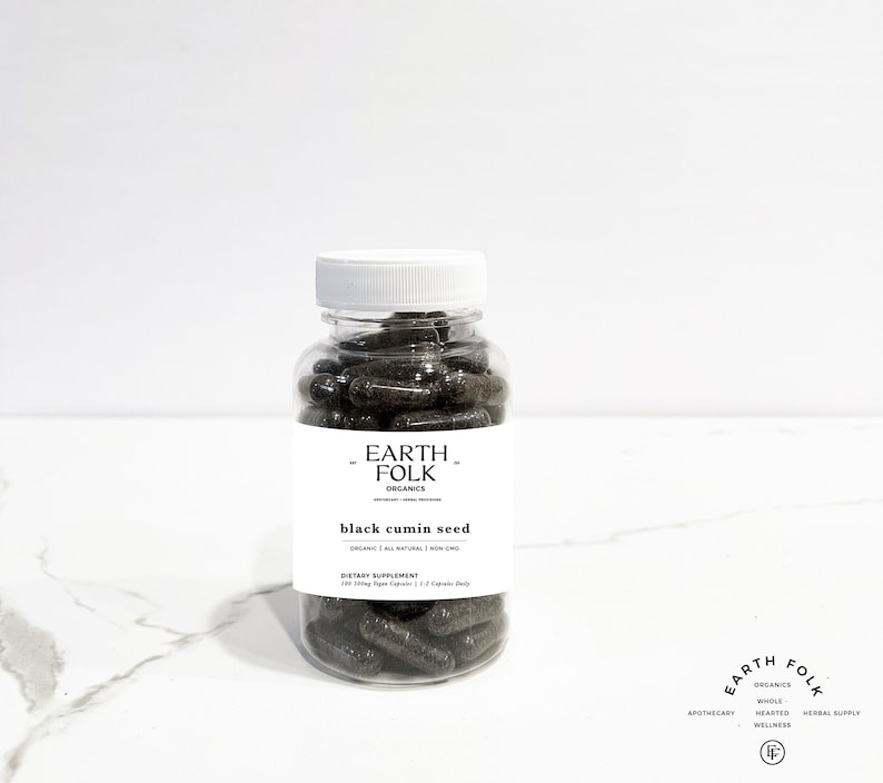 May include: A clear glass bottle filled with black capsules labeled "EARTH FOLK ORGANICS black cumin seed ORGANIC | ALL NATURAL | NON GMO DIETARY SUPPLEMENT 120 500mg Vegan Capsules / 2 Capsules Daily"