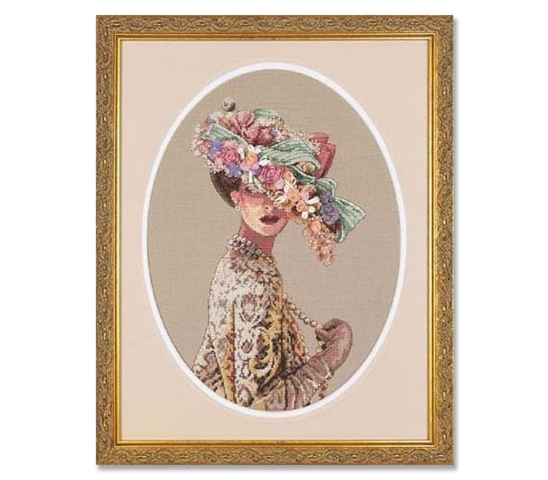 May include: A framed cross-stitch embroidery of a woman wearing a large, floral hat. The hat is made of pink, purple, and white flowers and green leaves. The woman is wearing a patterned dress and a pearl necklace.